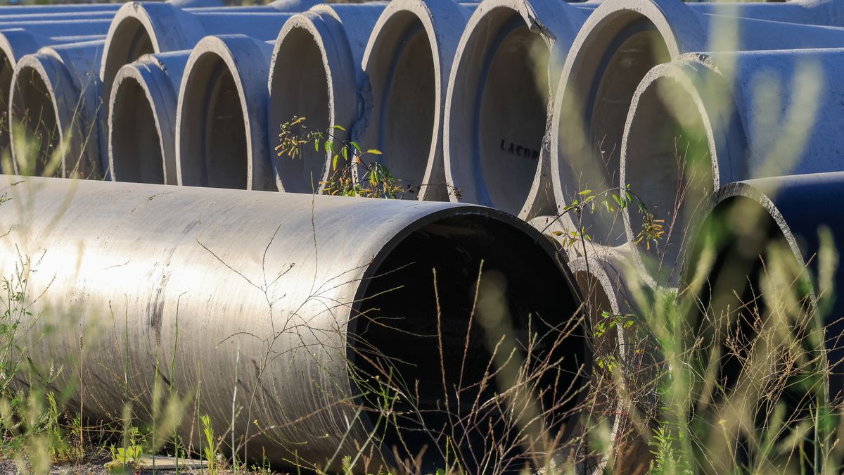 Stacked concrete pipes in an outdoor storage area surrounded by grass
