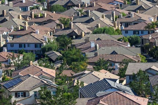 Aerial shot of a sunlit residential area showcasing tiled rooftops and lush greenery.
