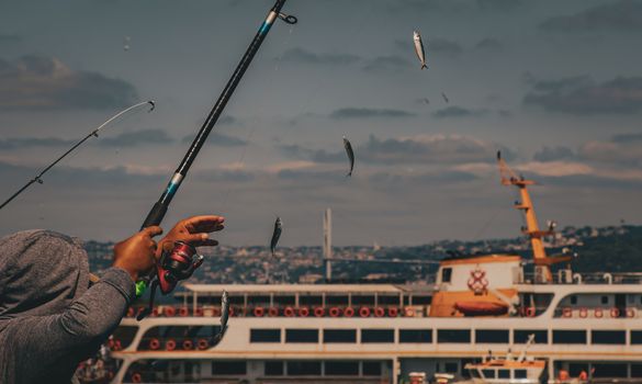 Fisherman casting line with fish near a ferry in Istanbul, showcasing a dynamic fishing scene.