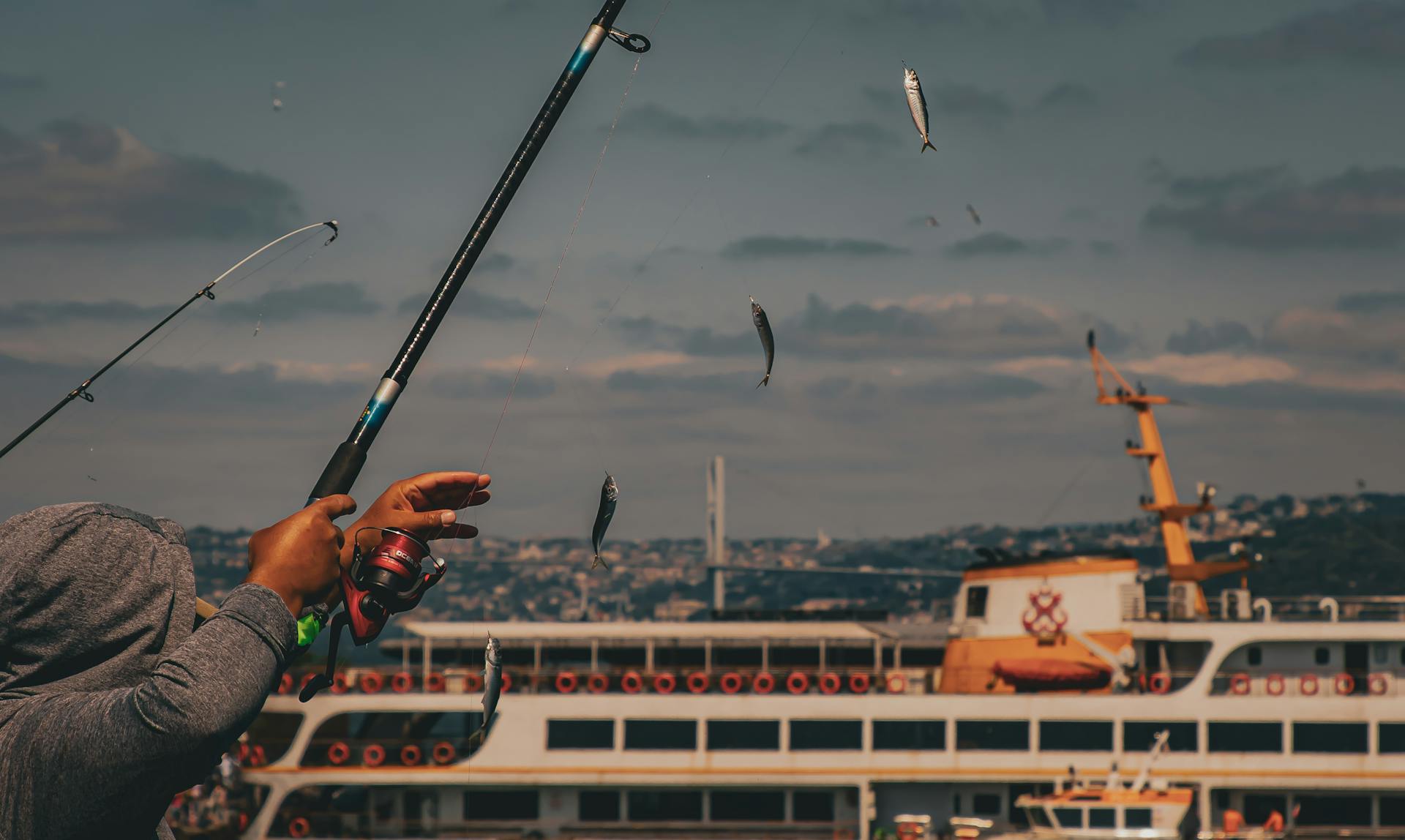Fisherman casting line with fish near a ferry in Istanbul, showcasing a dynamic fishing scene.