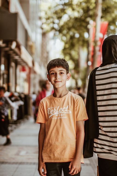 Free Teenage boy in a casual t-shirt standing on a busy urban walkway in daylight. Stock Photo