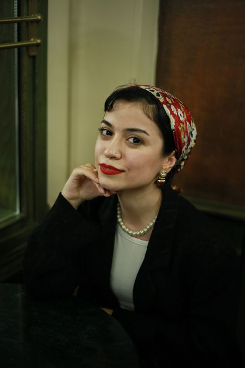 Free Portrait of a woman with a floral headscarf and pearls, elegantly posing in a cafe. Stock Photo