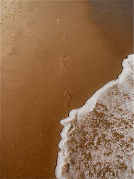Footprints on a sandy beach with gentle waves approaching the shore.