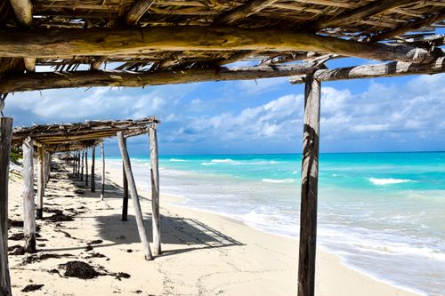 Free Serene Santa Marta beach along Cuba’s coast with rustic wooden shade structures and clear turquoise waters. Stock Photo