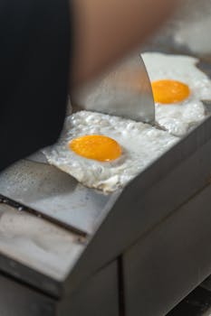 Detailed shot of a fried egg being cooked on a stainless steel griddle by a professional chef.