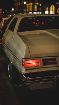 Rear view of a vintage car parked on a city street at night, showcasing urban nightlife ambiance.