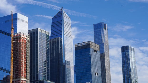 Iconic New York City skyline featuring modern glass and steel skyscrapers against a bright blue sky.