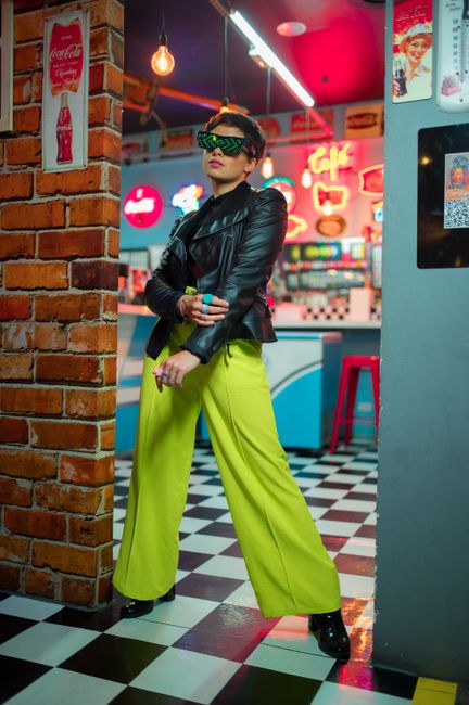 Fashionable woman in leather jacket and neon pants in a vibrant retro diner.