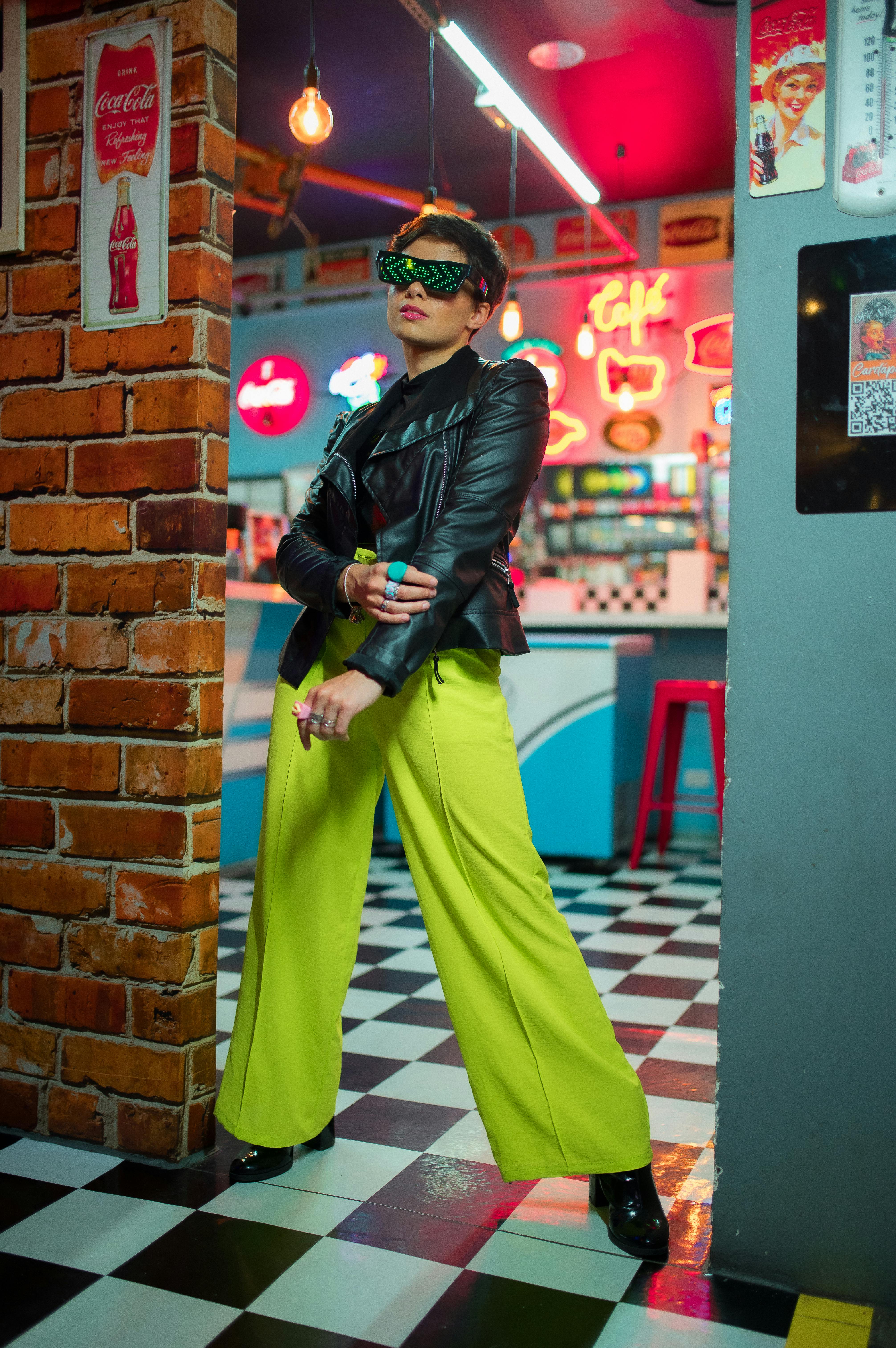 Free Fashionable woman in leather jacket and neon pants in a vibrant retro diner. Stock Photo