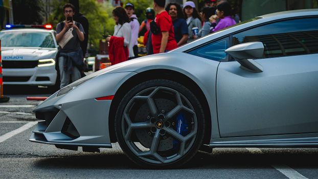 Close-up of a silver sports car with people and a police car in the background.