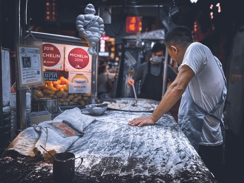 Street food vendor preparing dough in a bustling night market in Bangkok, Thailand.
