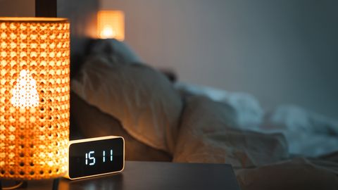 A warm, inviting bedroom with a glowing lamp and digital alarm clock reading 15:11.