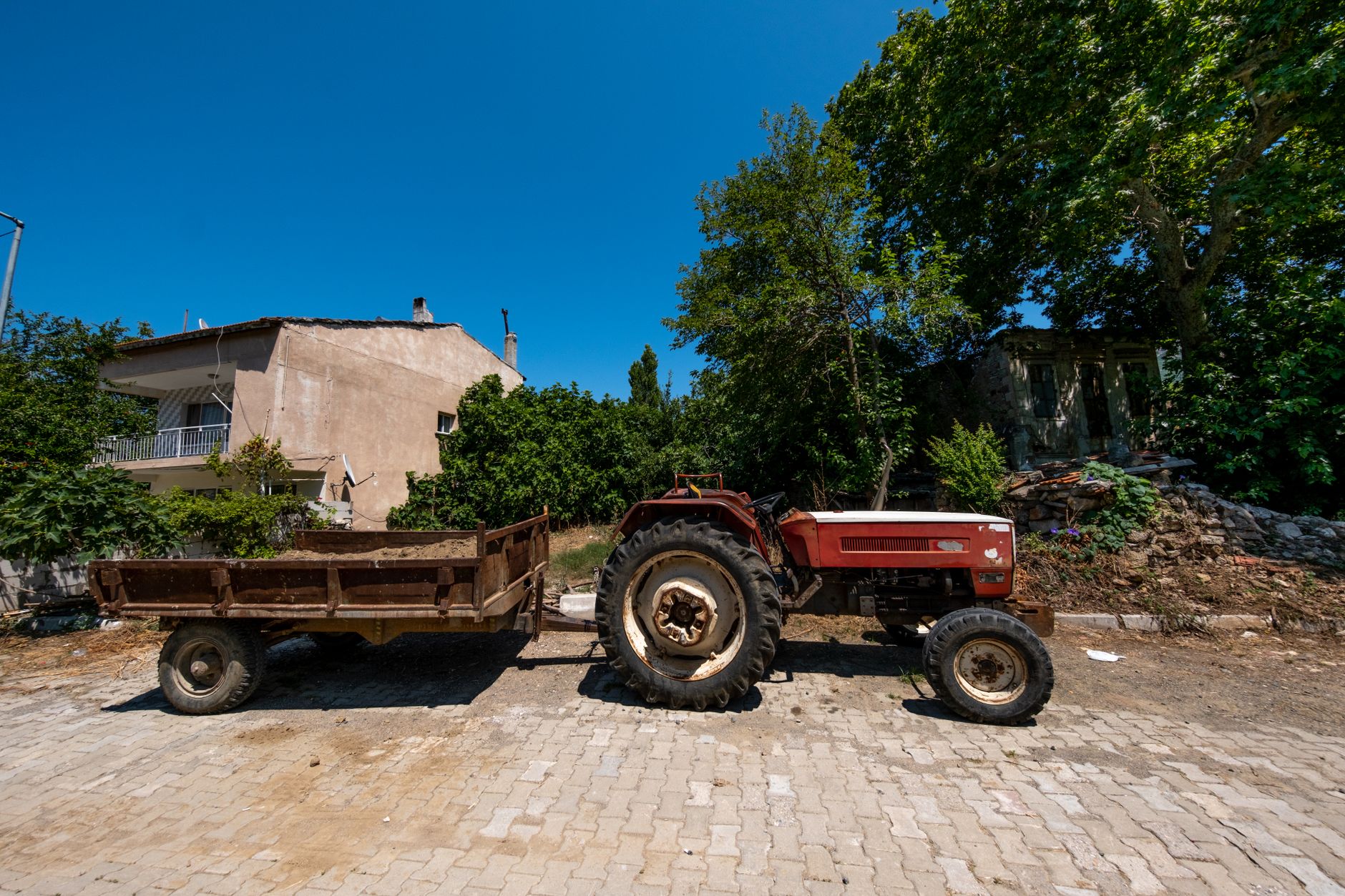 A vintage tractor with trailer parked in a sunny rural area in Foça, İzmir, Türkiye, showcasing agricultural life.