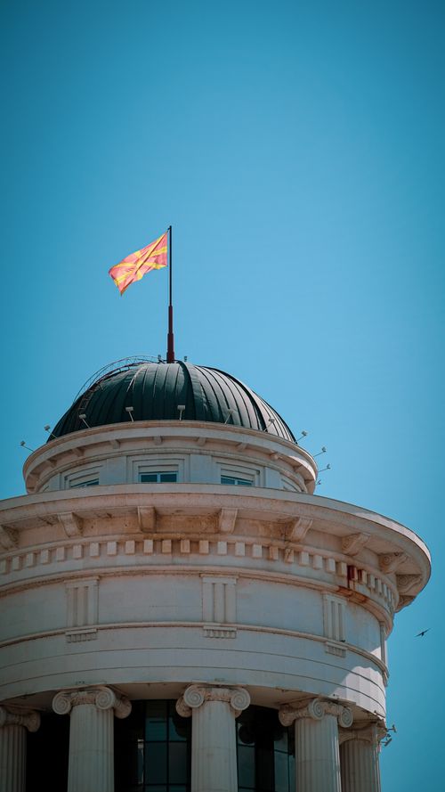 Free Vertical shot of a classical dome with the Macedonian flag against a clear blue sky. Stock Photo
