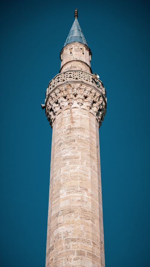 Free A detailed view of a sunlit mosque minaret against a clear blue sky, showcasing Islamic architecture. Stock Photo