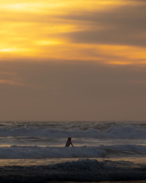 Free A woman enjoys a tranquil sunset at the beach, surrounded by gentle sea waves. Stock Photo