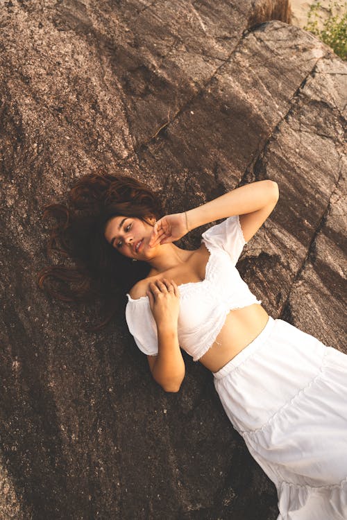 Woman in White Top and Skirt Lying Down on Rock