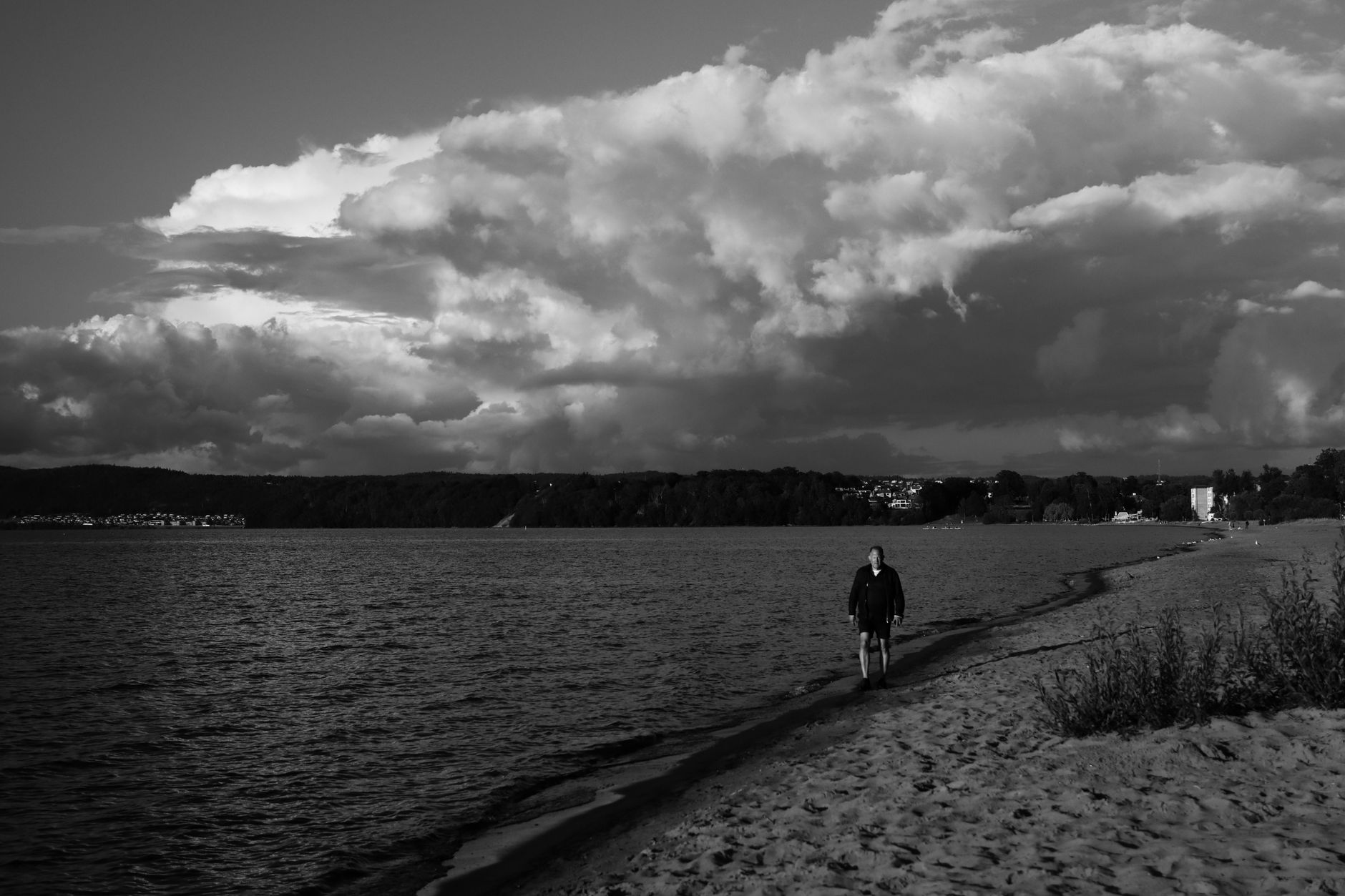 A man walks along a Swedish beach under a dramatic sky. Captured in black and white.