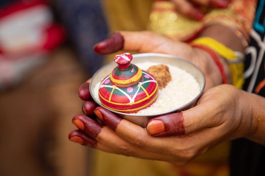 Close-up of henna-decorated hands holding a bowl with decorative figurine, highlighting cultural significance.