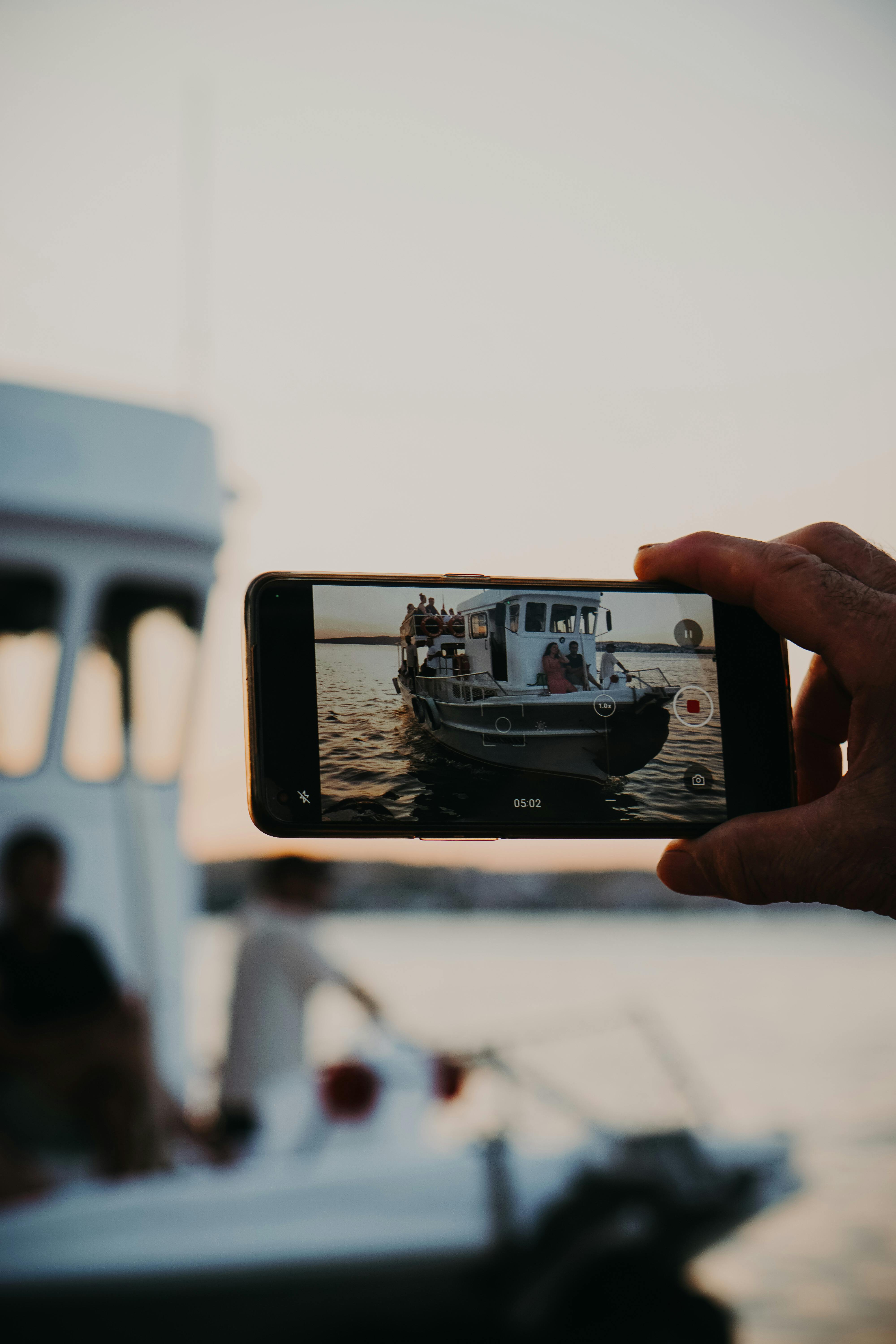 man hand holding smartphone and recording video of motorboat