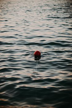 A solitary red buoy floats gently on the wavy lake at sunset in Ayvalık, Balıkesir, Türkiye.