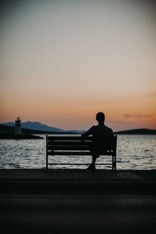 Free A man sits on a bench overlooking the sea at sunset in Ayvalık, Turkey. Stock Photo