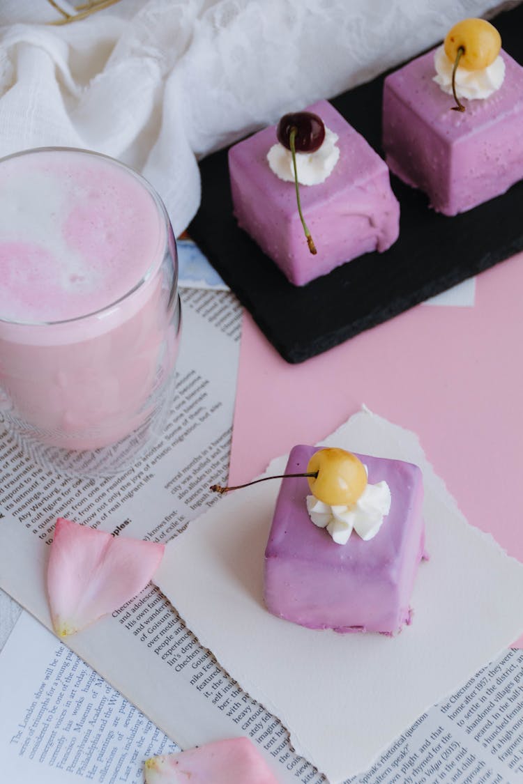 Lilac Colored Cake With Yellow Cherry On Top And A Pink Fruit Milkshake