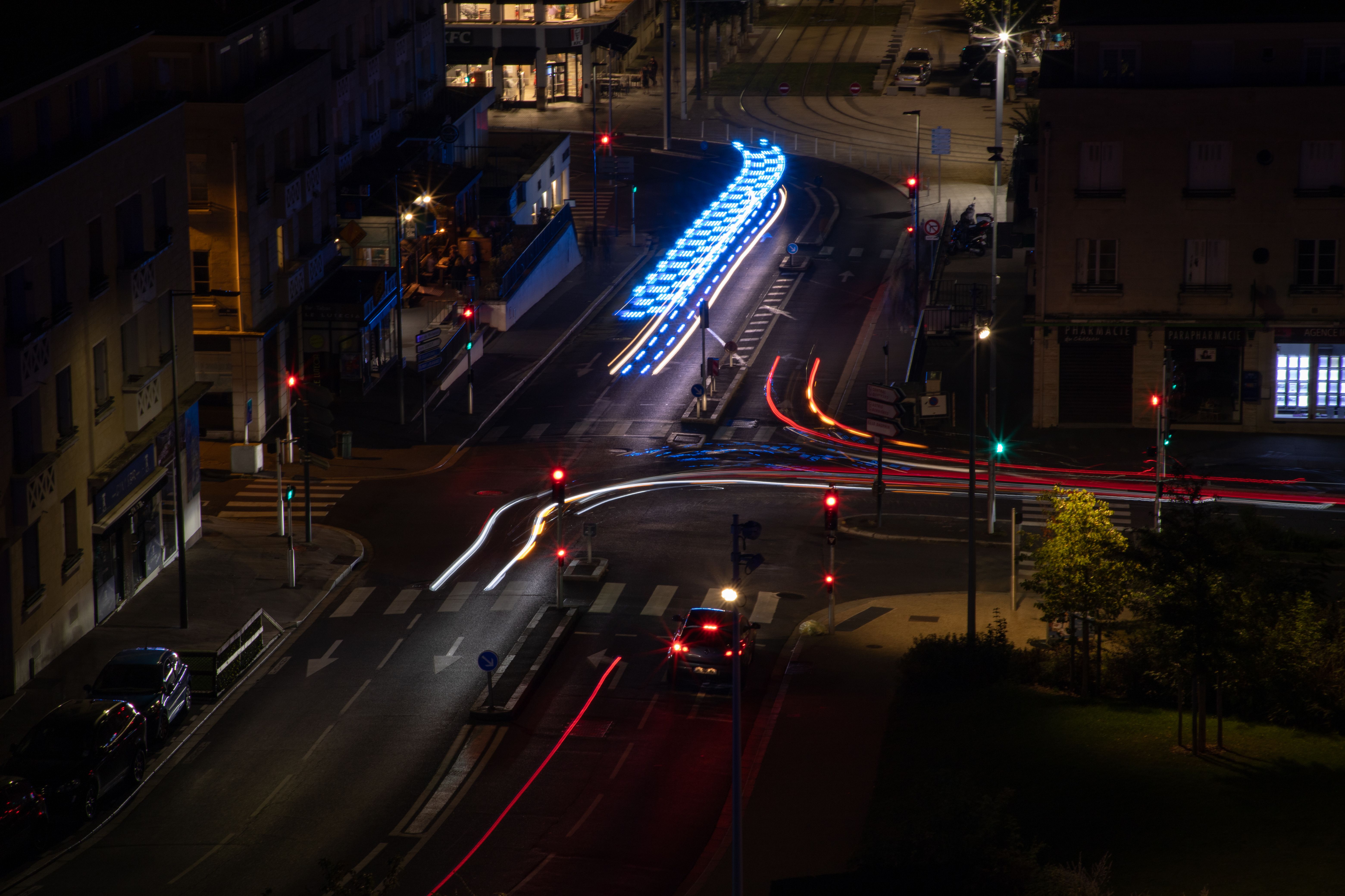Vue aérienne des rues illuminées de Caen la nuit, mettant en valeur des traînées lumineuses colorées et l'architecture urbaine.