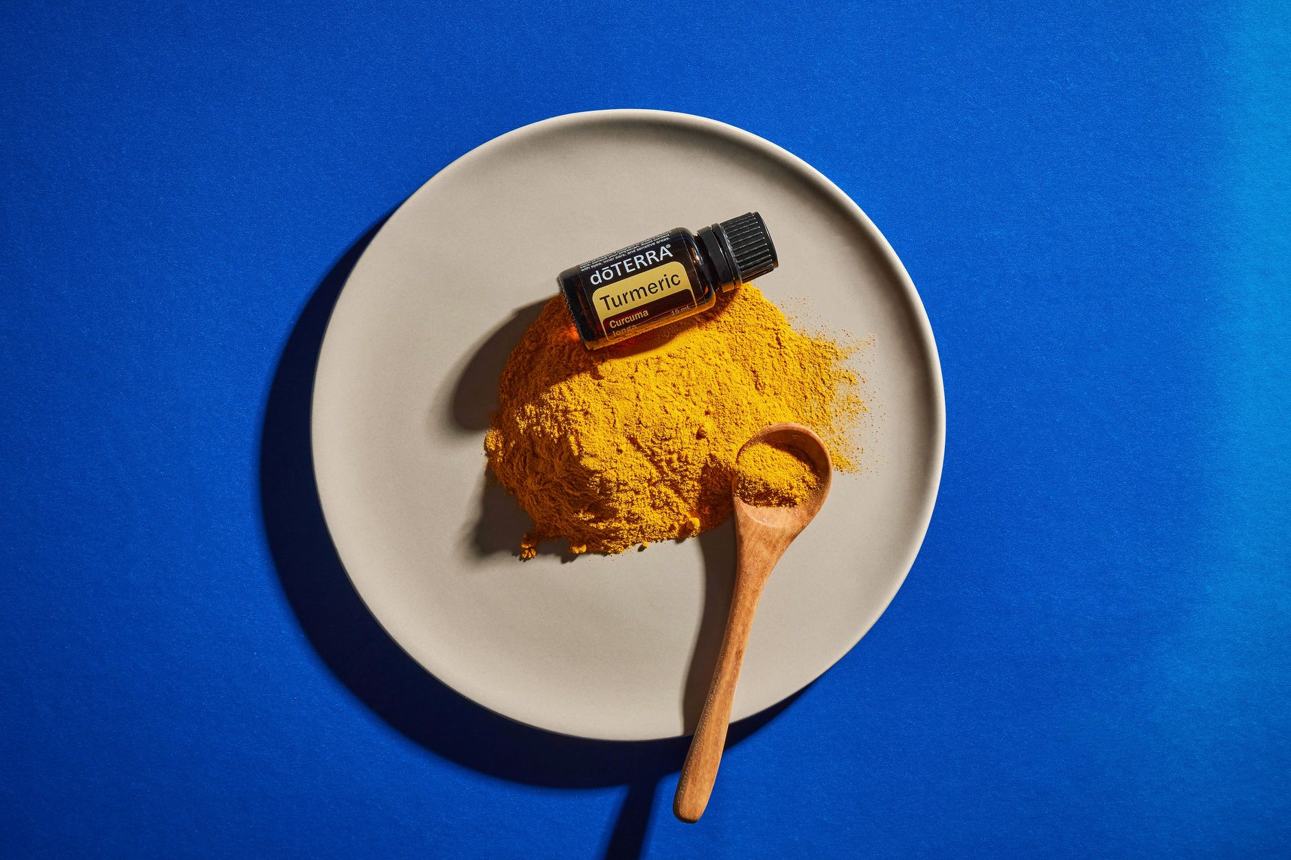 Flat lay of turmeric powder with essential oil on a plate, set against a vibrant blue background.
