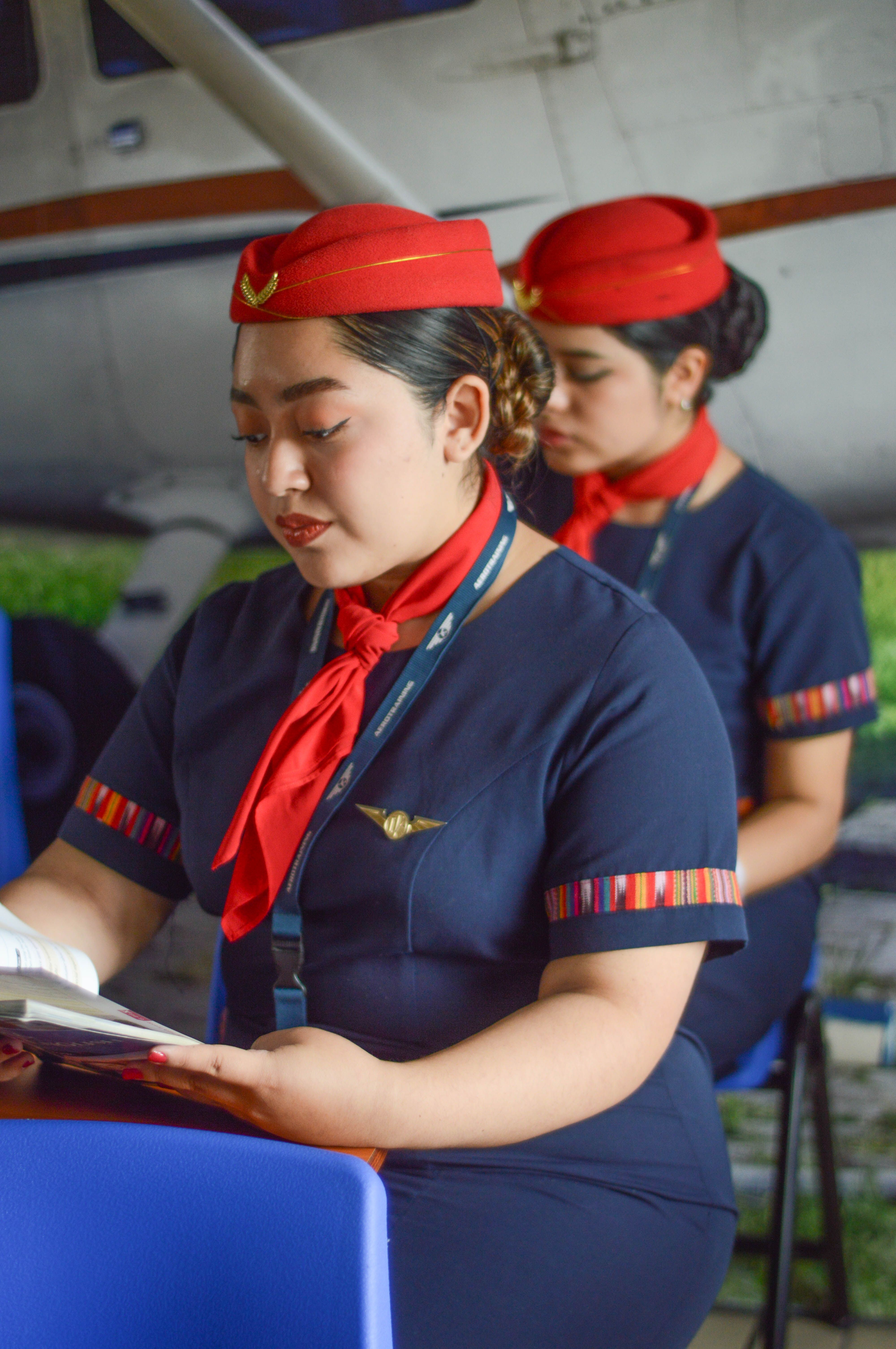 Two flight attendants in elegant uniforms reading onboard an aircraft.
