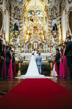 A bride and groom stand elegantly before an ornate altar in São João del Rei, Brazil.