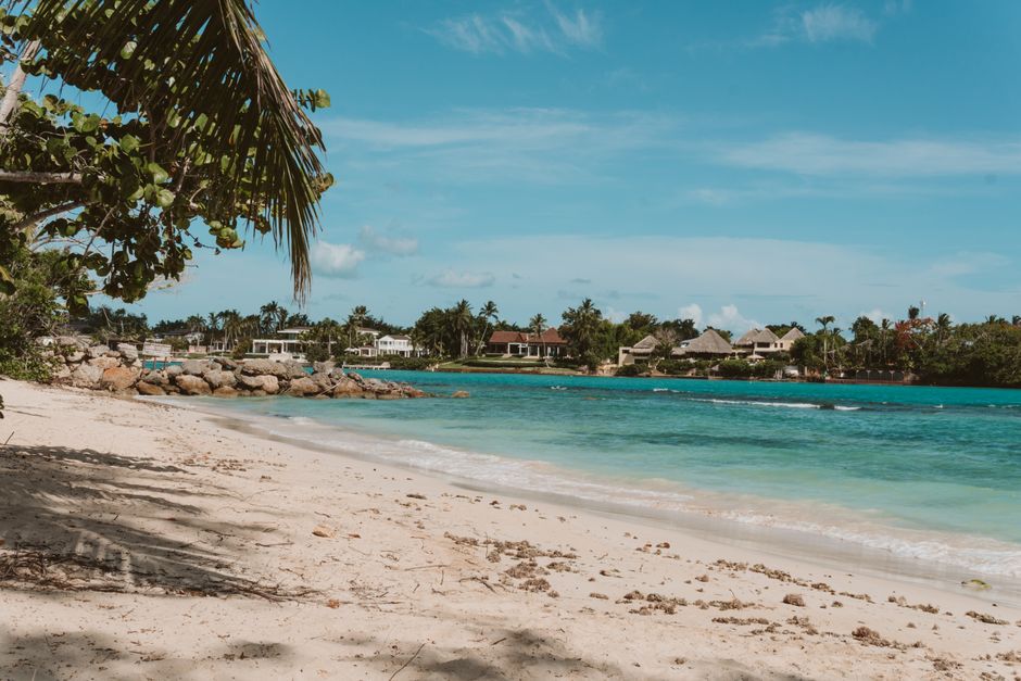 Scenic view of a tranquil tropical beach with palm trees and clear turquoise water under a sunny sky.