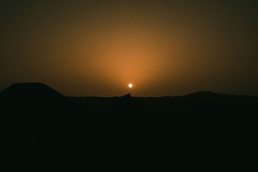 A tranquil sunset over the desert landscape in Ouargla, Algeria, with a warm orange horizon.