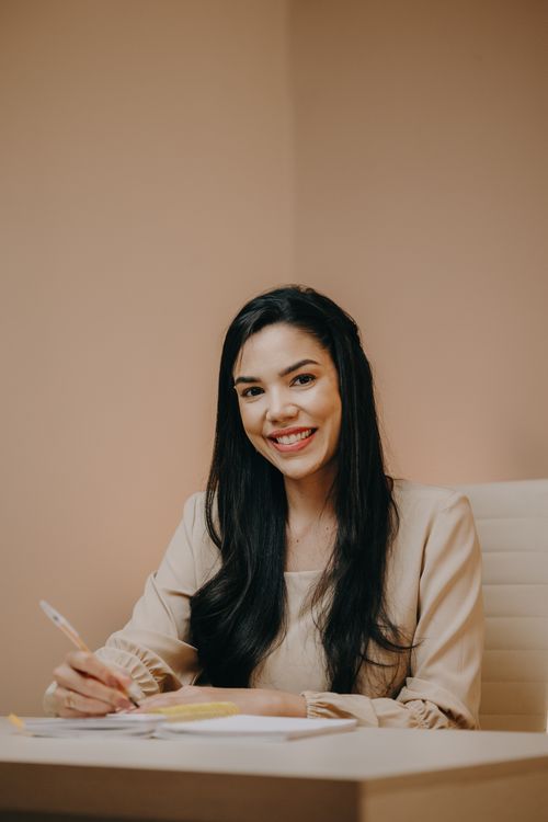 Free A young woman smiles confidently while writing at her desk in an elegant office setting. Stock Photo