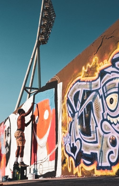 Free Street artist paints vibrant graffiti on outdoor wall under sunlight. Urban creativity in action. Stock Photo