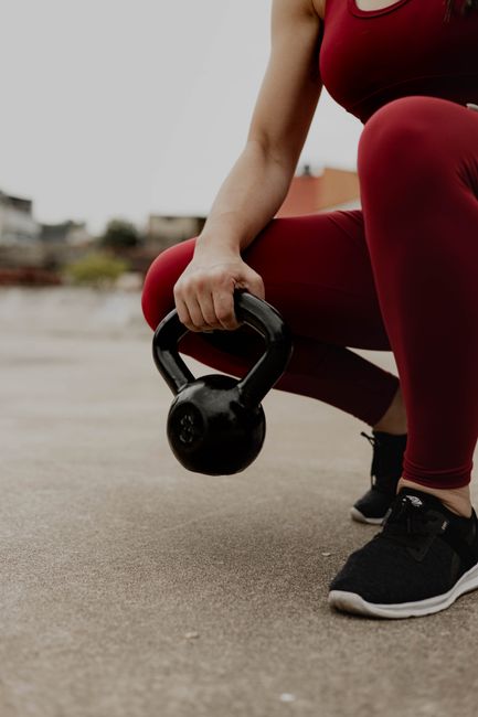Close-up of a woman in red activewear holding a kettlebell on pavement during a workout.