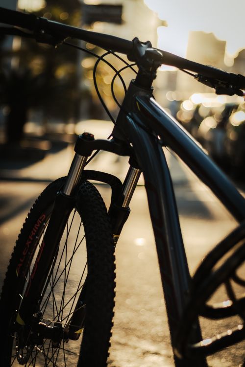 Free Moody silhouette of a bicycle at sunset in an urban setting, with cars in the background. Stock Photo