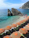 意大利海岸上，彩色的海滩伞与岩石结构相映成趣，碧绿的大海波光粼粼