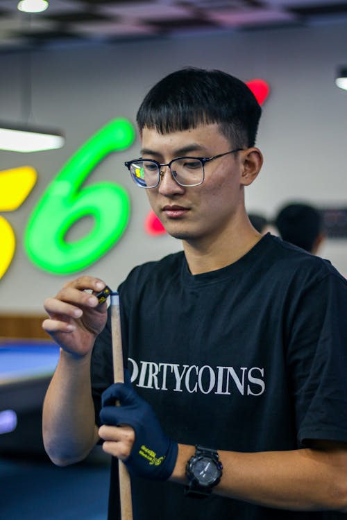 Young Man Putting Chalk on the Cue Tip during a Billiard Game 