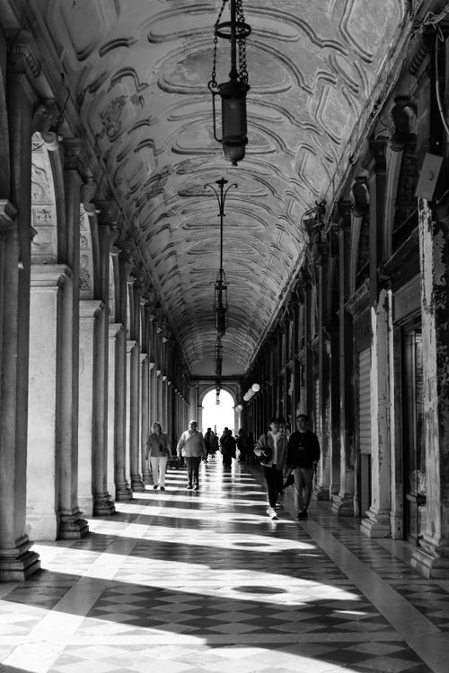 Free A classic black and white photo of a colonnade in Venice, Italy, showing people walking. Stock Photo