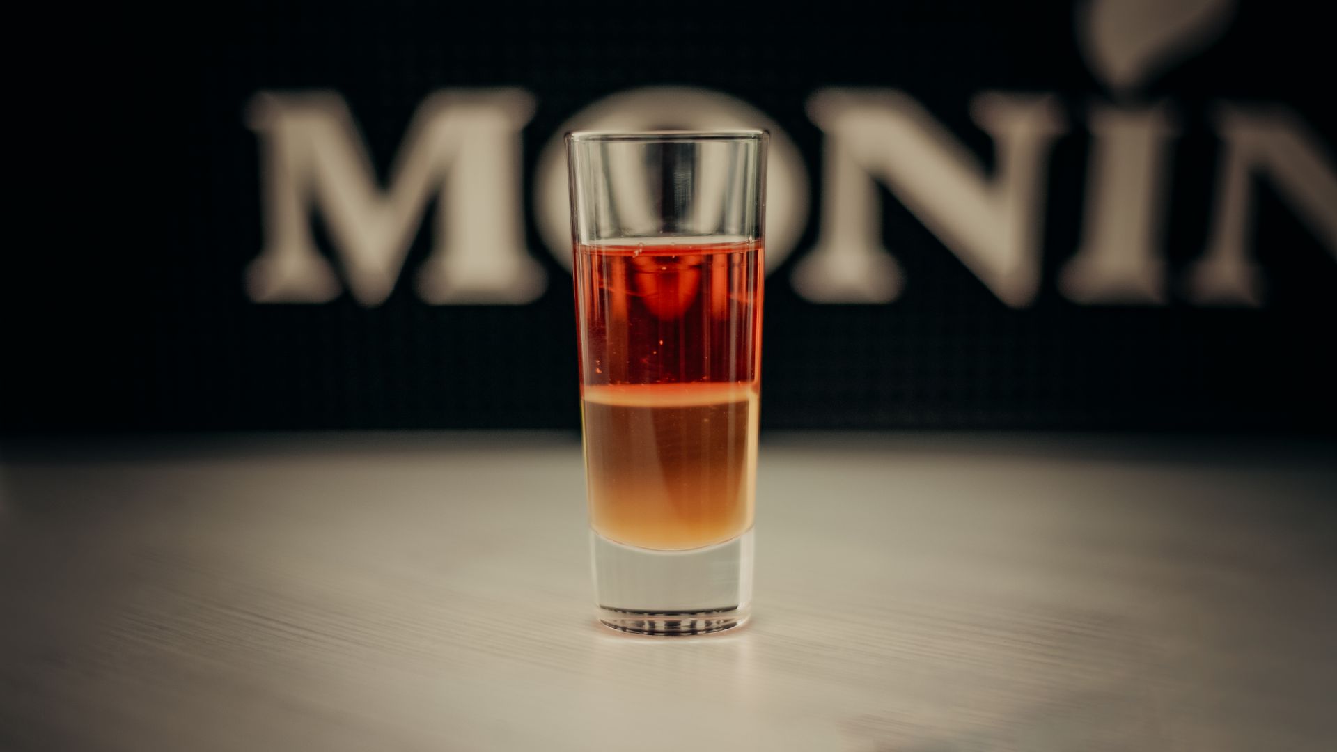 Close-up of a layered shot drink in a glass, with sharp focus and blurred background.