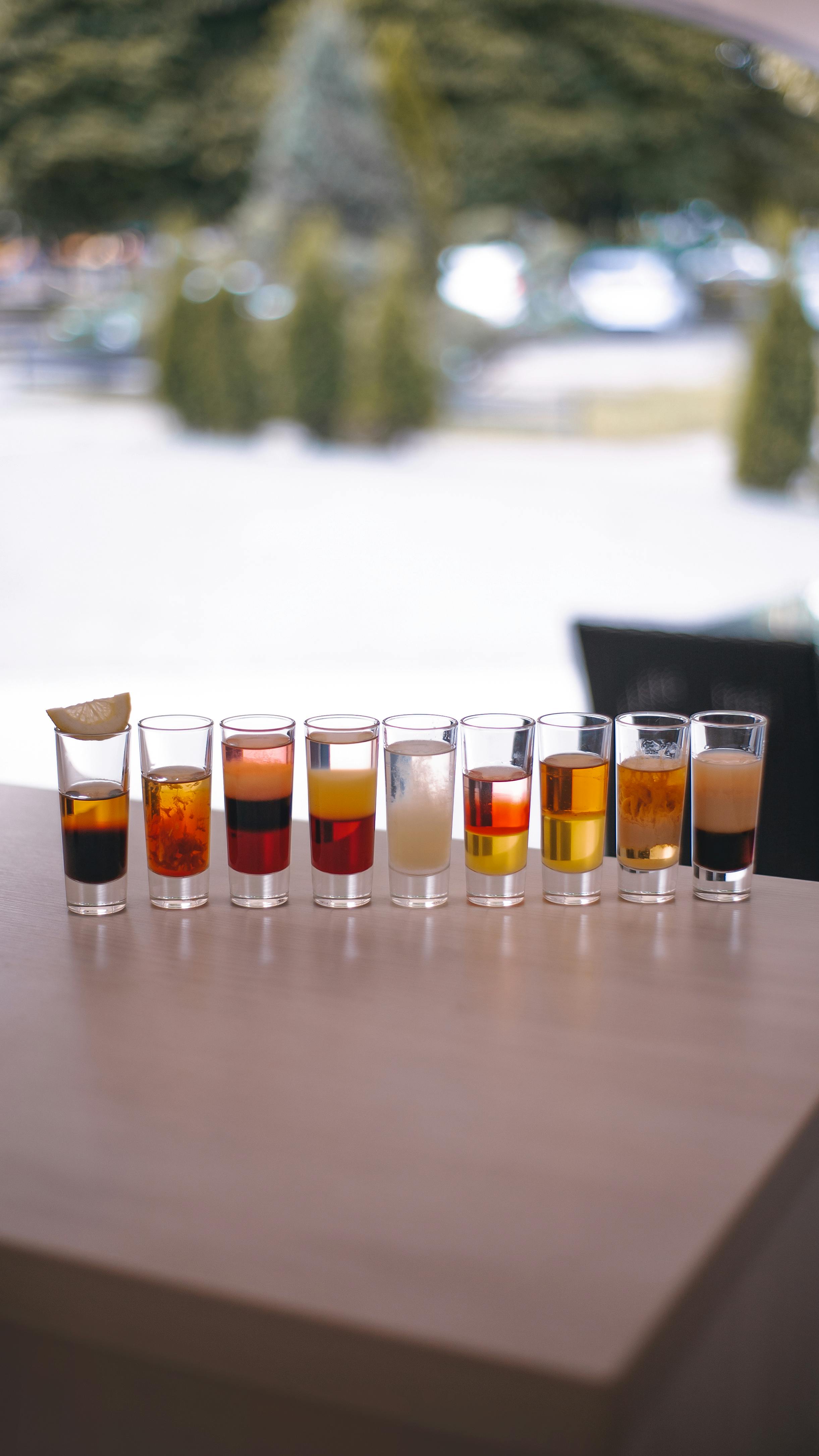 A vibrant array of mixed drinks in shot glasses on a wooden table.