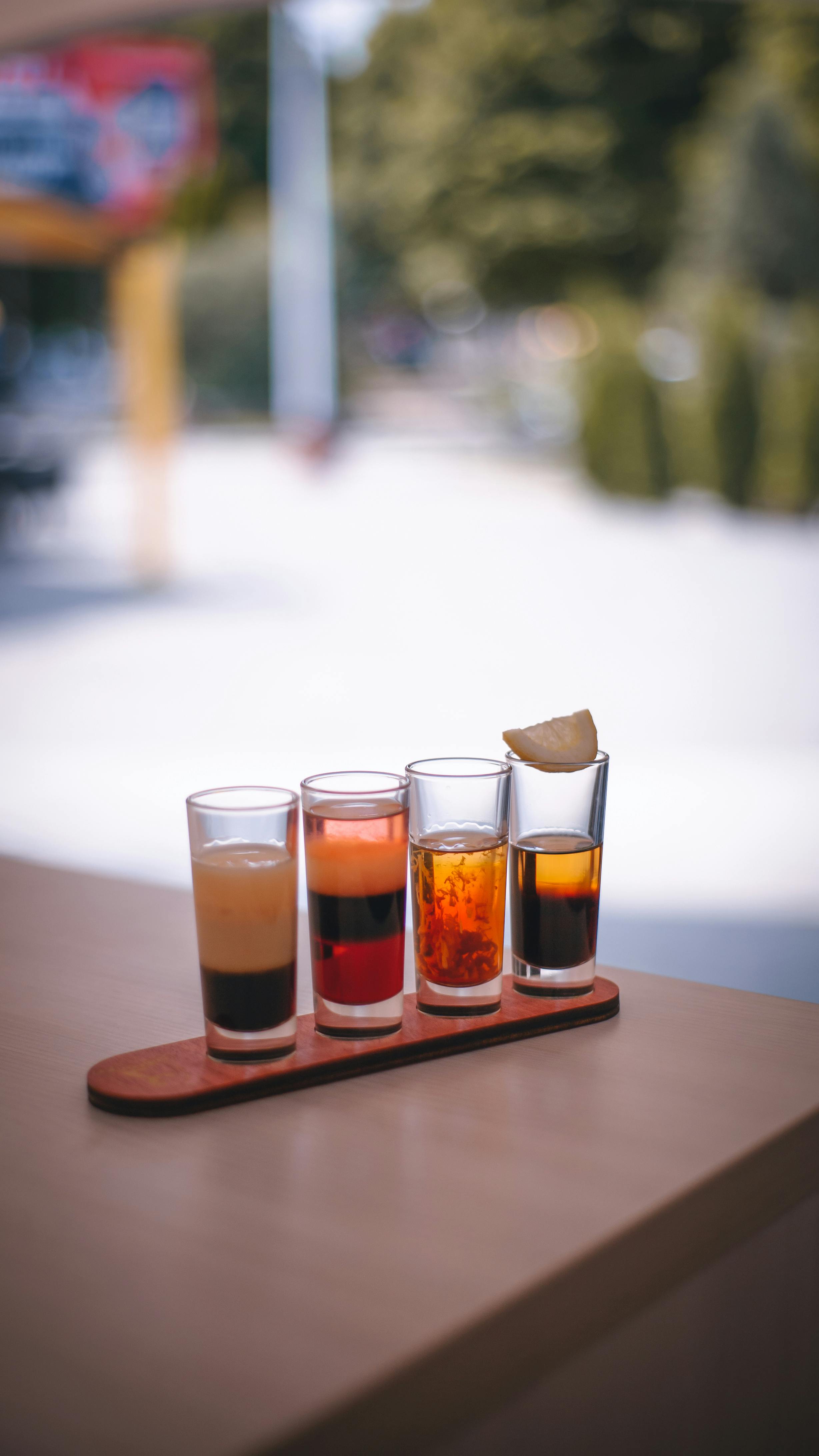 A selection of colorful alcoholic shots displayed on a wooden rack with a blurred outdoor background.