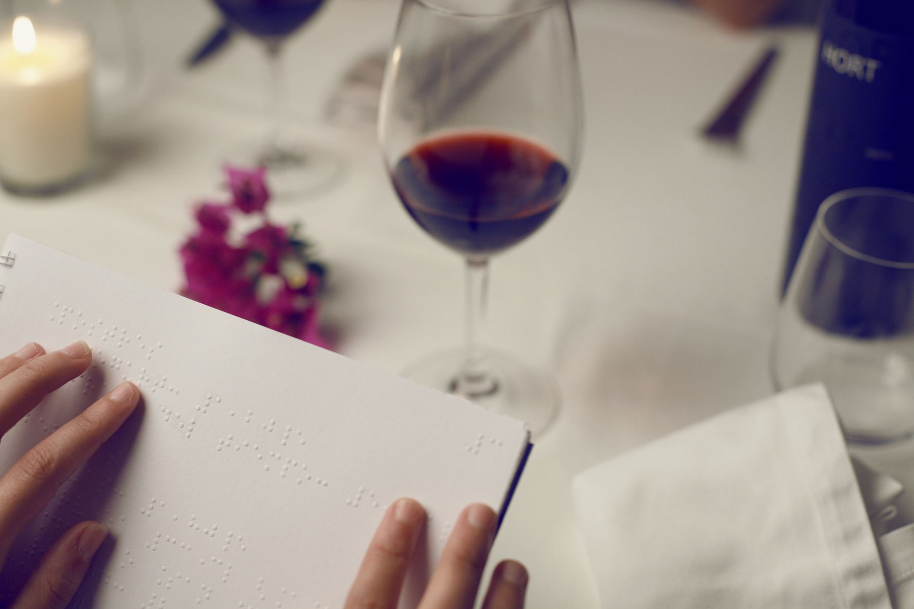 A close-up of a braille menu at a sophisticated restaurant setting with wine.