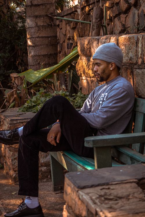 Free Man in beanie sitting on a green bench outdoors, relaxed and thoughtful. Stock Photo