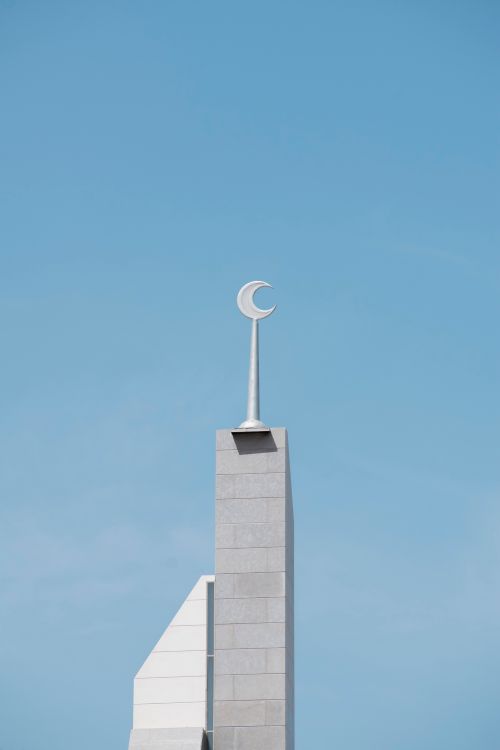 Free A minimalist view of a mosque minaret featuring a crescent symbol against a clear blue sky. Stock Photo