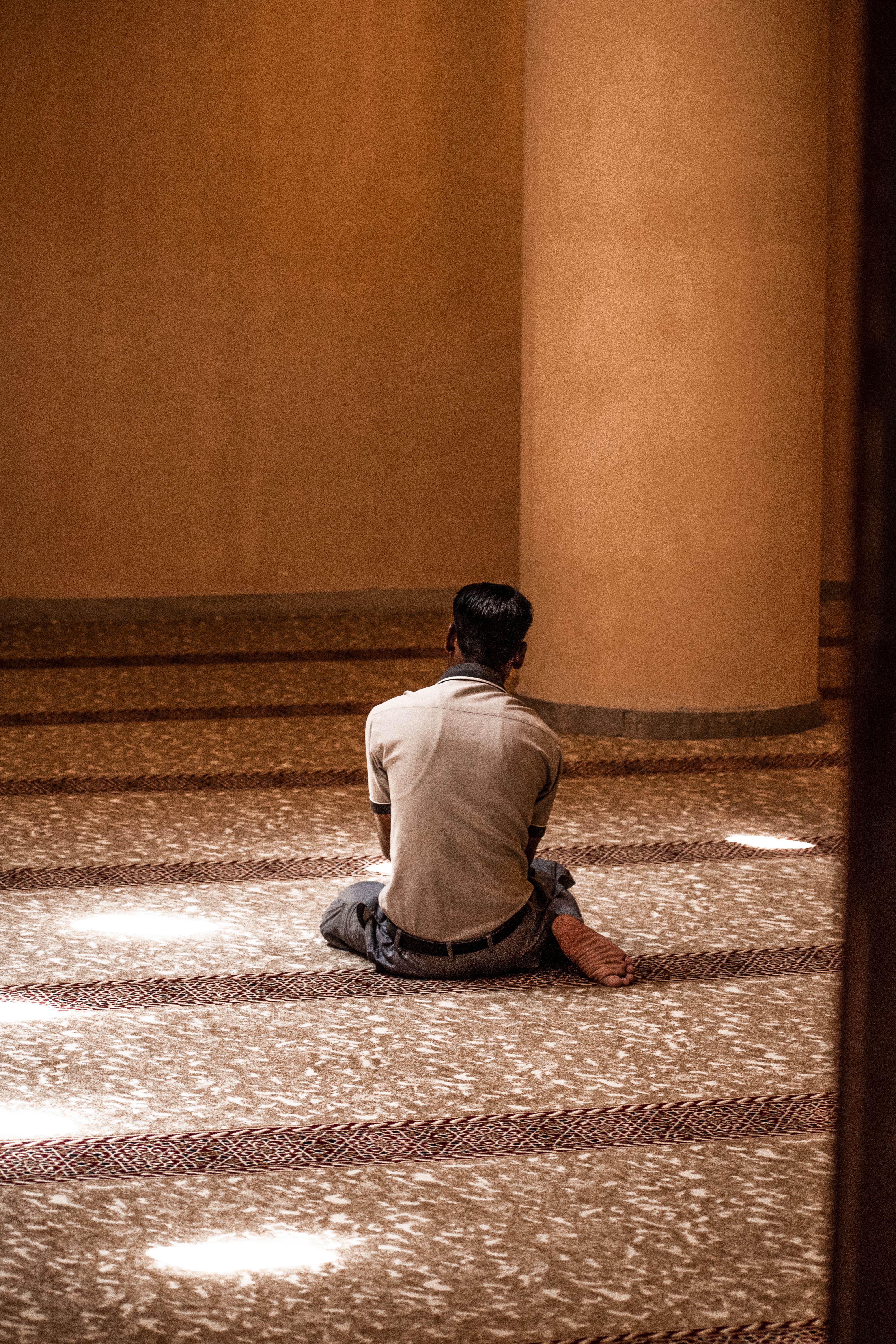 A man sits quietly while praying indoors, capturing a serene religious moment.