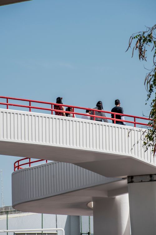 Free A group of people walking on a modern urban footbridge under clear blue skies, offering a unique architectural view. Stock Photo
