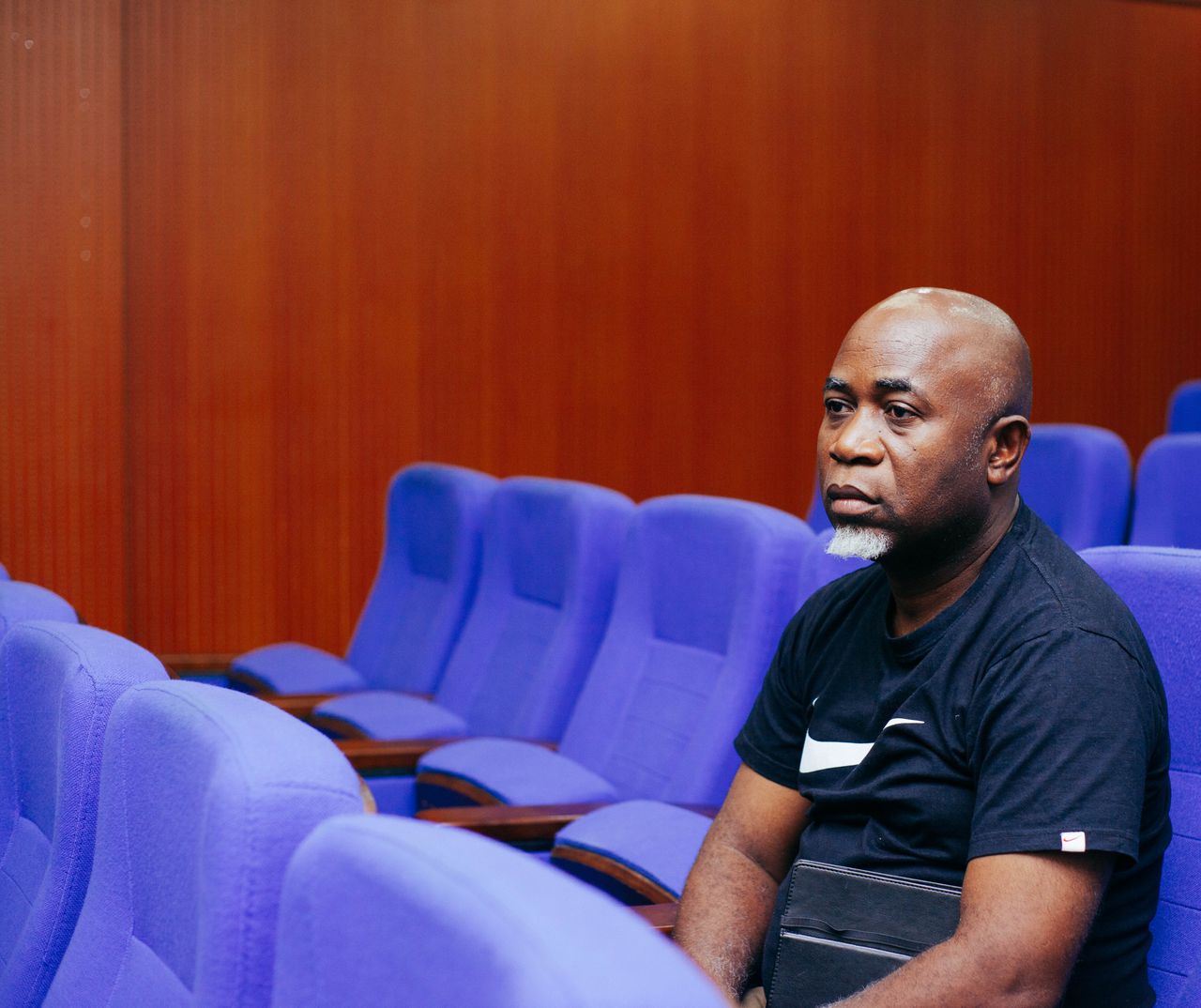 a man in a black t shirt sits alone in a theater with blue seats