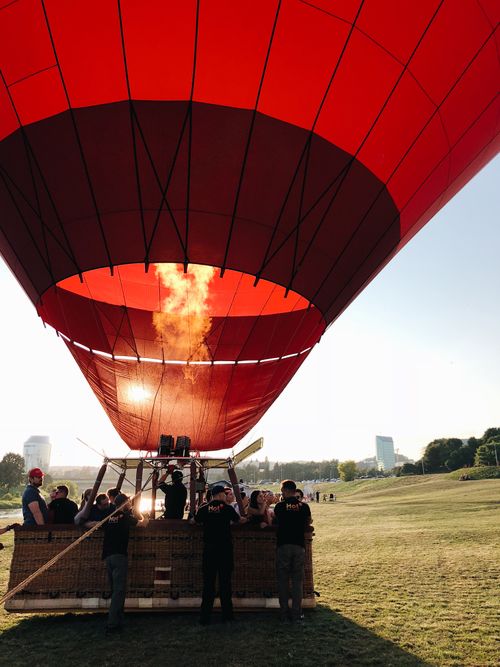 Free Vibrant hot air balloon in flight over grassy field with people enjoying the ride. Stock Photo